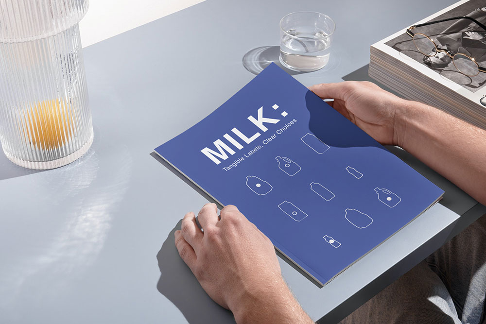 A blue book with the title Milk. The book is set on a desk and is held by a pair of hands.